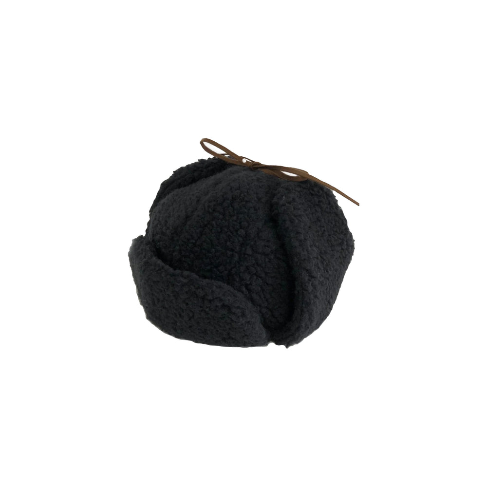 The Boa Aviator Hat by Cableami is a black, textured hat made of soft cotton Boa fleece with ear flaps and a small brown bow. It offers adjustable sizing for warmth and comfort, perfect for winter days against a pristine white background.