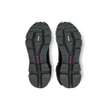 The image displays the black treaded soles of a pair of Women's Cloudrock 2 Waterproof athletic shoes by On Running, viewed from below, featuring colored accents in green and purple.