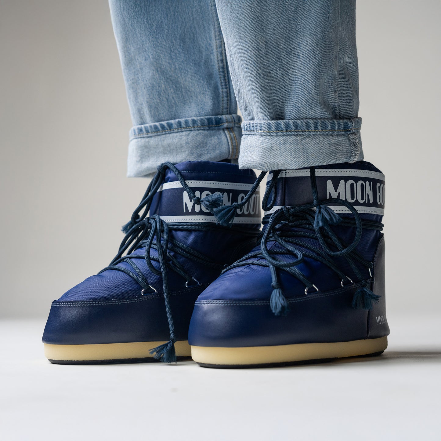 A person wearing Moon Boot's Icon Low Nylon, Blue boots, perfectly paired with light blue jeans. These stylish water-repellent boots add flair and functionality to any adventure.