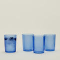 The Hawkins New York Essential Glassware (Set of 4) Large showcases four blue borosilicate glasses, three empty and one filled with ice cubes and berries. Their retro-inspired, stackable design is perfect for any modern kitchen setup.