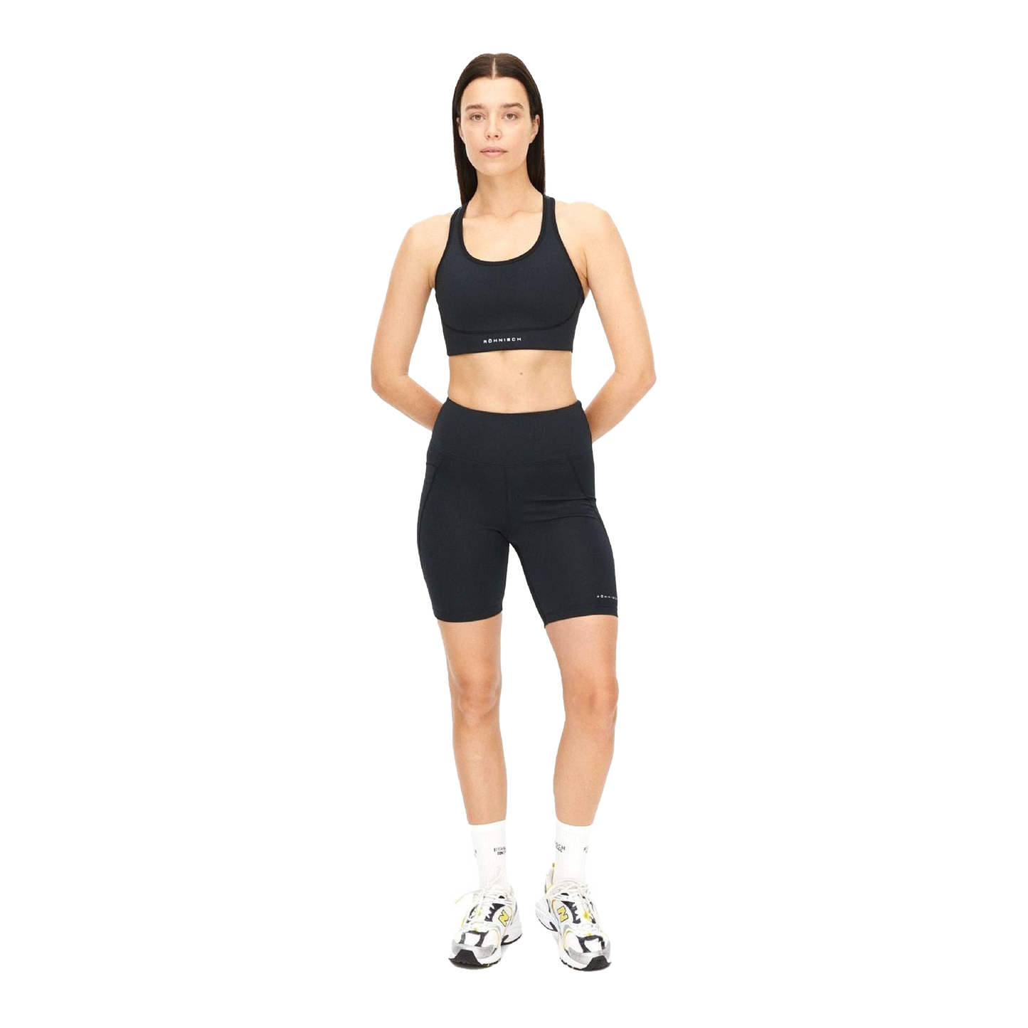 A person wearing Rohnisch's Flattering High Waist Bike Tights in black, paired with white sneakers, stands against a clear background. The tights are made from recycled polyester.