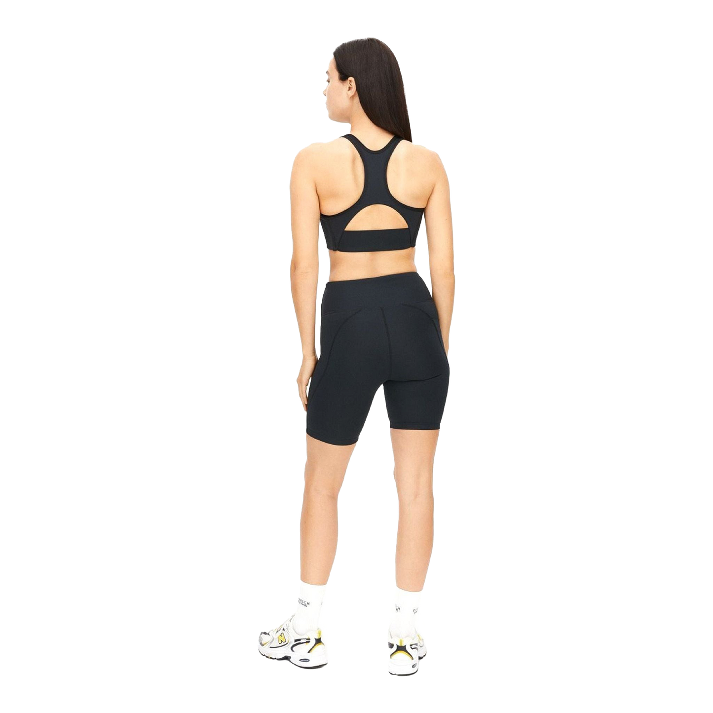 A person facing away from the camera wears a black sports bra and Rohnisch's Flattering High Waist Bike Tights, crafted from recycled polyester, complemented by white socks and sneakers.