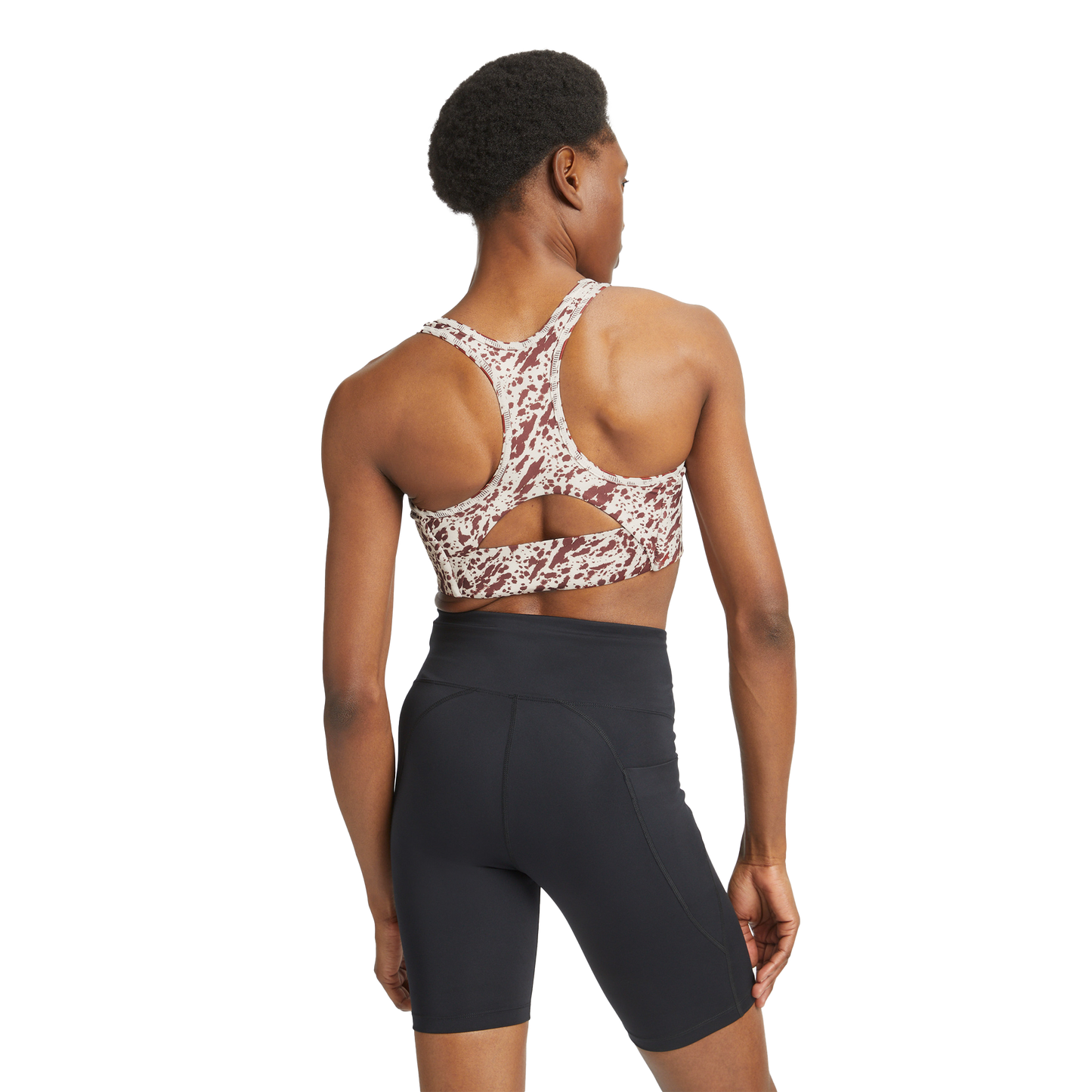 A person wearing a Rohnisch Flattering Sports Bra with a racerback design and moisture-wicking pattern, paired with black athletic shorts, stands facing away.