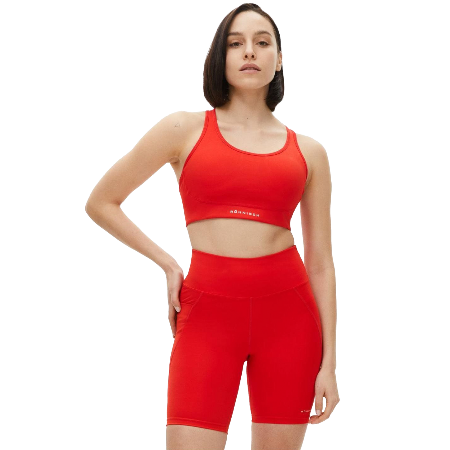 Dressed in a Rohnisch Flattering Sports Bra and matching shorts, the person stands confidently with one hand on their hip, gazing ahead. The moisture-wicking fabric ensures comfort as they pursue their fitness goals.