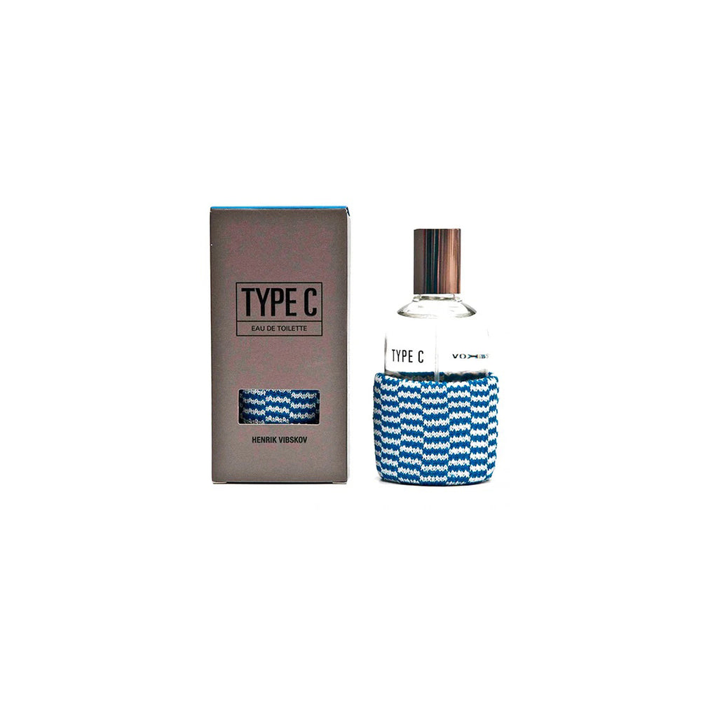 A bottle of Henrik Vibskov's Type-C Eau de Toilette, blending sea breeze notes, is elegantly displayed next to its matching box encased in a blue patterned sleeve.