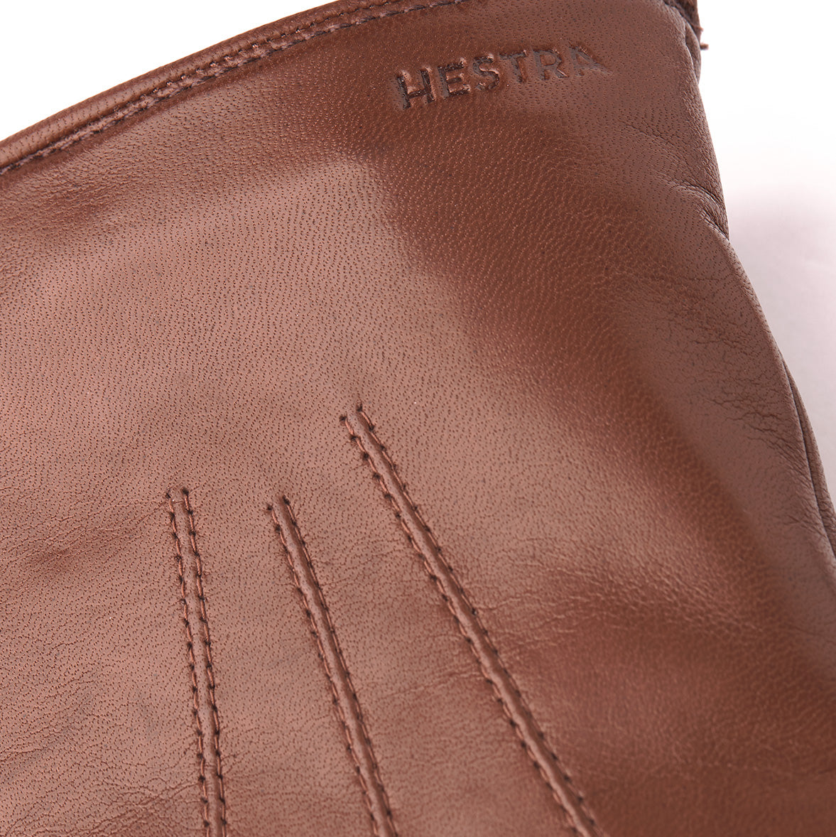 Close-up of the Nelson glove in chestnut, crafted from luxurious Italian lamb nappa with stitched detailing. The brand "Hestra" is embossed on the cuff, and its plush wool lining ensures warmth and comfort.