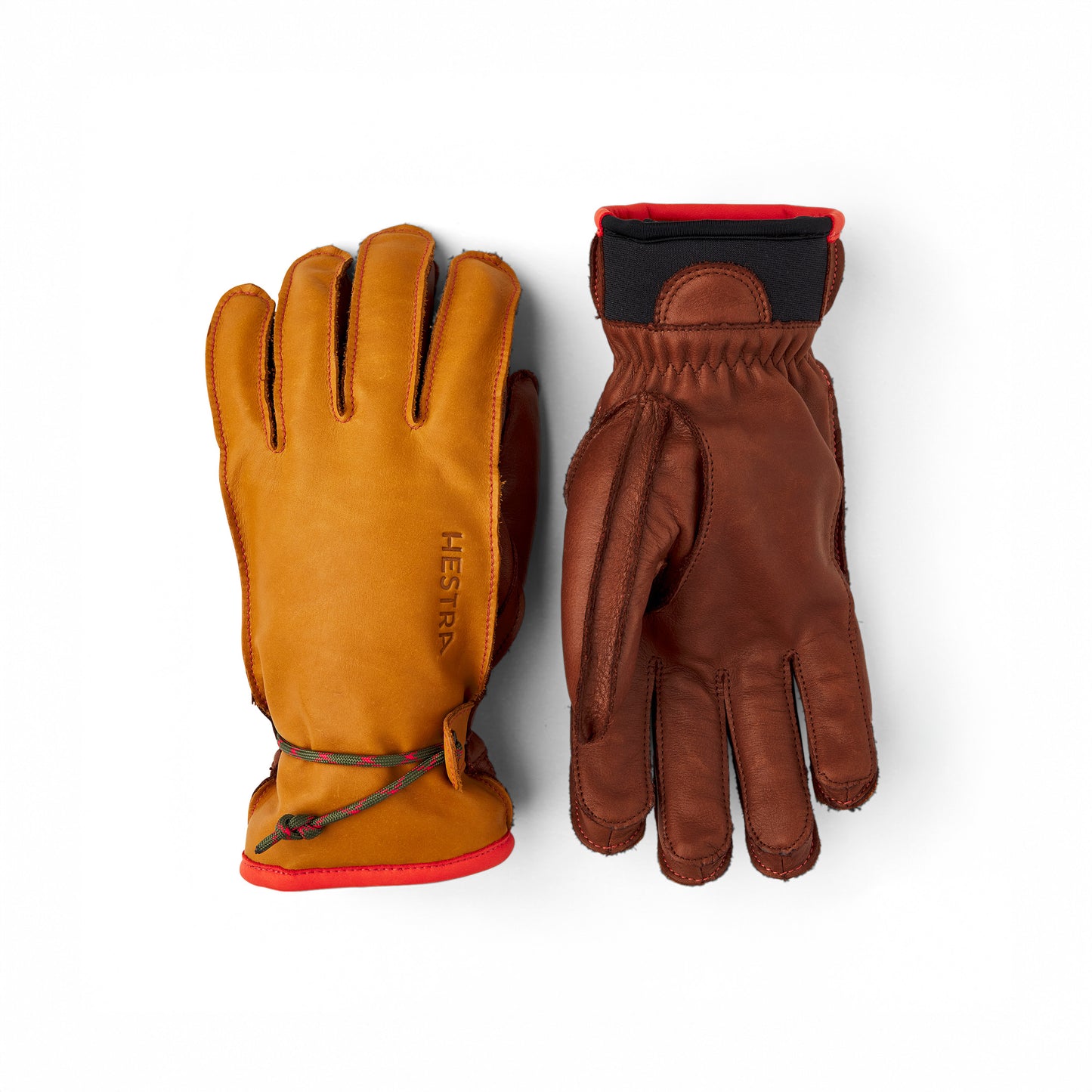 The Hestra Wakayama gloves in cork/brown are crafted from cowhide leather, featuring red trim and a branded logo on the left glove's palm-down, ski-glove design with a cinch cord. The right glove is shown palm-up. These gloves are perfect for the slopes with their removable liners.