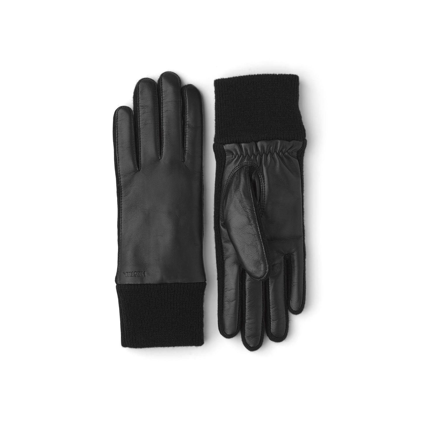 A pair of Hestra's Jeanne gloves, crafted from Italian lamb nappa with wool jersey cuffs, is shown on a white background. One glove stands upright while the other shows its palm-side.