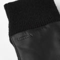 The Jeanne black glove by Hestra is made from luxurious Italian lamb nappa leather, features a ribbed knit cuff, and has "HESTRA" embossed on the surface.