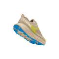 The Hoka W Stinson ATR 6, DOTN, in beige and lime green with blue sole accents, delivers versatile comfort for any workout. Against a white backdrop, it's perfect for those desiring both style and functionality.