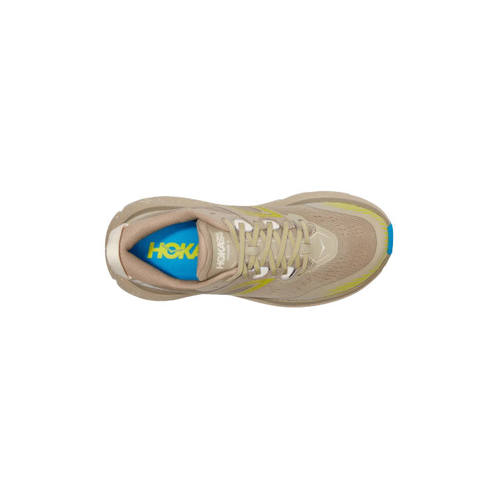 Top view of a Hoka W Stinson ATR 6, DOTN running shoe in beige with green and blue accents and visible laces, showcasing versatile comfort on a white background.