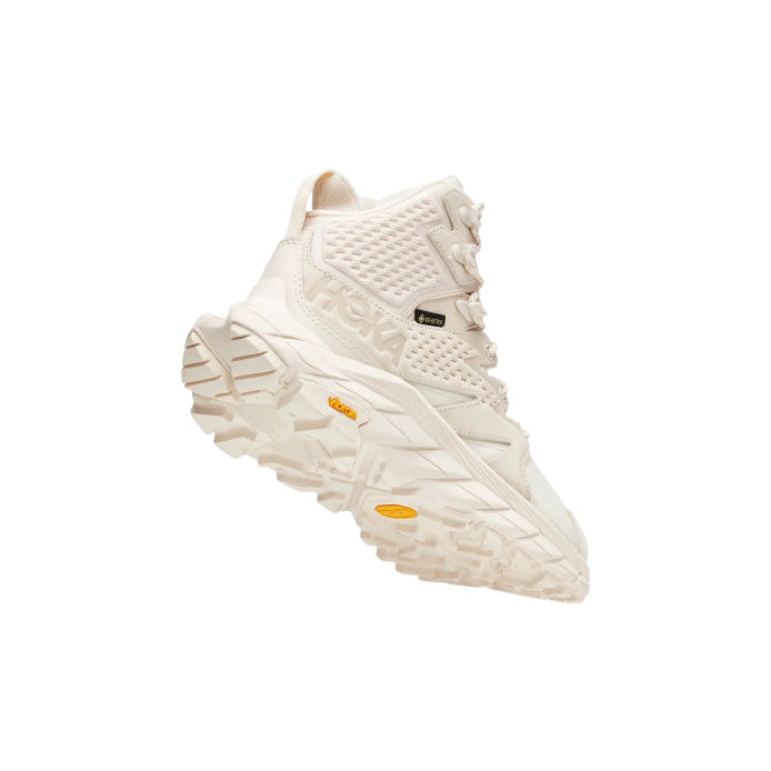 The Hoka W Anacapa MID GTX in Eggnog/Shifting Sand is an off-white high-top sneaker featuring lightweight leather, a rugged sole, and mesh panels for trail traction, shown at an angle.