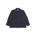 The Jungle Jacket by Universal Works is a dark blue utility jacket featuring a collared neck, long sleeves, and multiple flap pockets on the front. Crafted from recycled polyester for sustainability, this piece mirrors the iconic design of an Army Tropical Uniform Jacket.