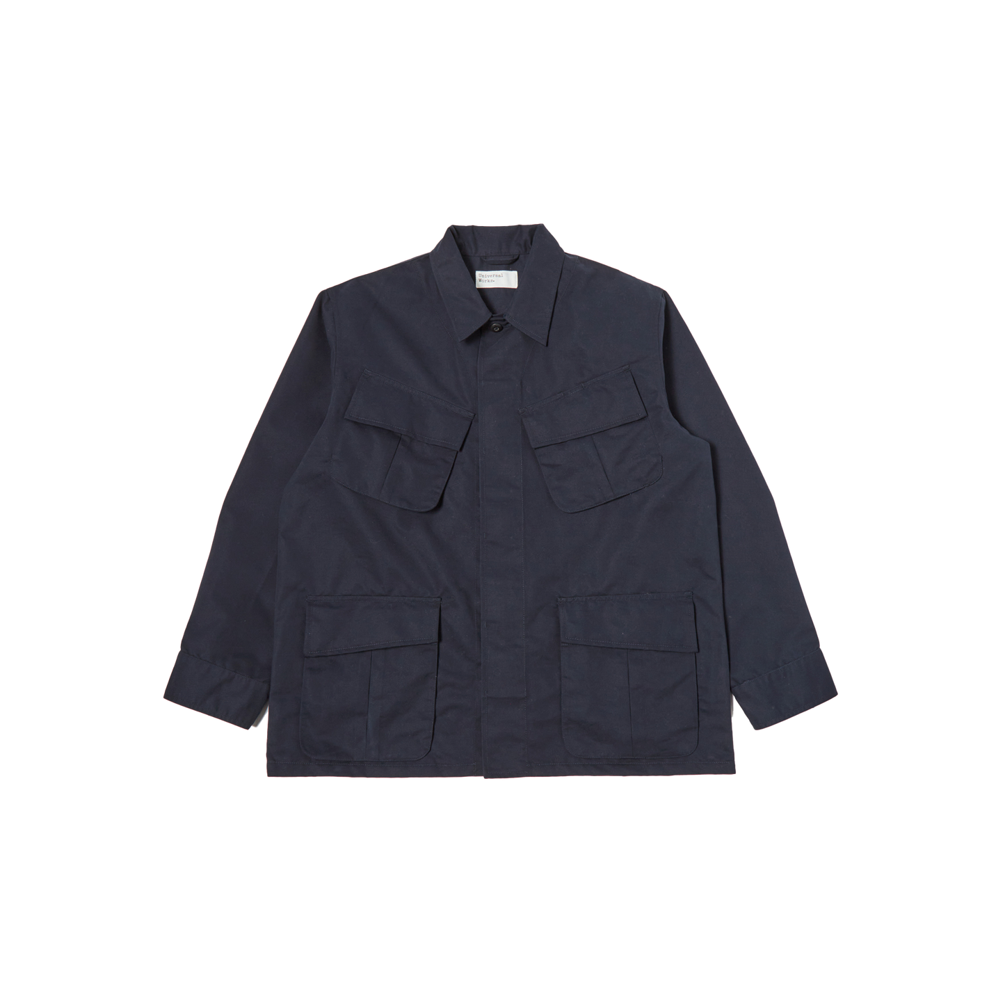 The Jungle Jacket by Universal Works is a dark blue utility jacket featuring a collared neck, long sleeves, and multiple flap pockets on the front. Crafted from recycled polyester for sustainability, this piece mirrors the iconic design of an Army Tropical Uniform Jacket.