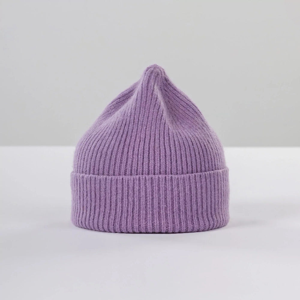 The Le Bonnet Lavender Beanie with a ribbed brim sits elegantly on a white surface, exuding cozy style.