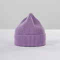 The Le Bonnet Lavender Beanie with a ribbed brim sits elegantly on a white surface, exuding cozy style.