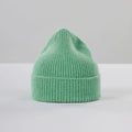 The "Beanie, Jade" by Le Bonnet is a mint green ribbed hat made from soft lambswool and stands upright on a plain light gray surface.