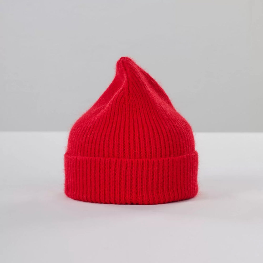 The Crimson Beanie by Le Bonnet evokes cozy Scottish winters with its pointed top, displayed on a neutral background.