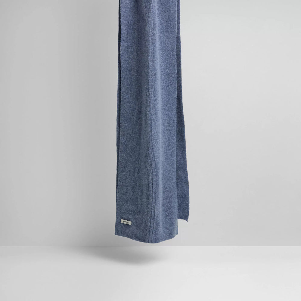 A Le Bonnet Washed Denim scarf, reminiscent of luxurious lambswool, is draped against a plain white background with a small tag near the bottom.