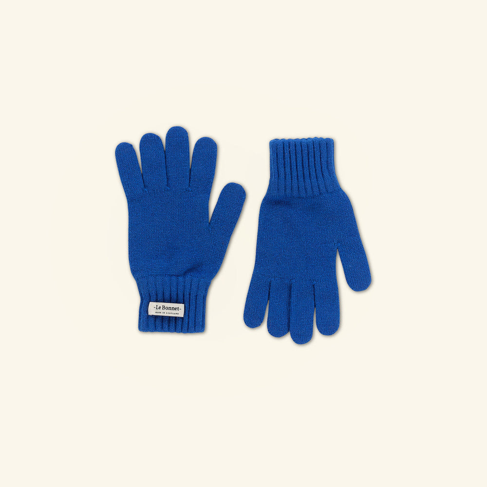 A cozy pair of Le Bonnet's Royal Azure knitted gloves, made from Merino wool for chilly days, feature ribbed cuffs and are shown on a neutral backdrop. A small label is visible near the wrist of one glove.