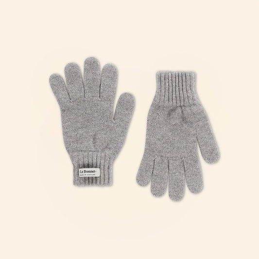 A pair of Le Bonnet's "Gloves, Smoke" crafted from merino wool with ribbed cuffs on a plain beige background. One glove is palm up, the other is palm down, and the label is visible—ideal for combining warmth and style on colder days.