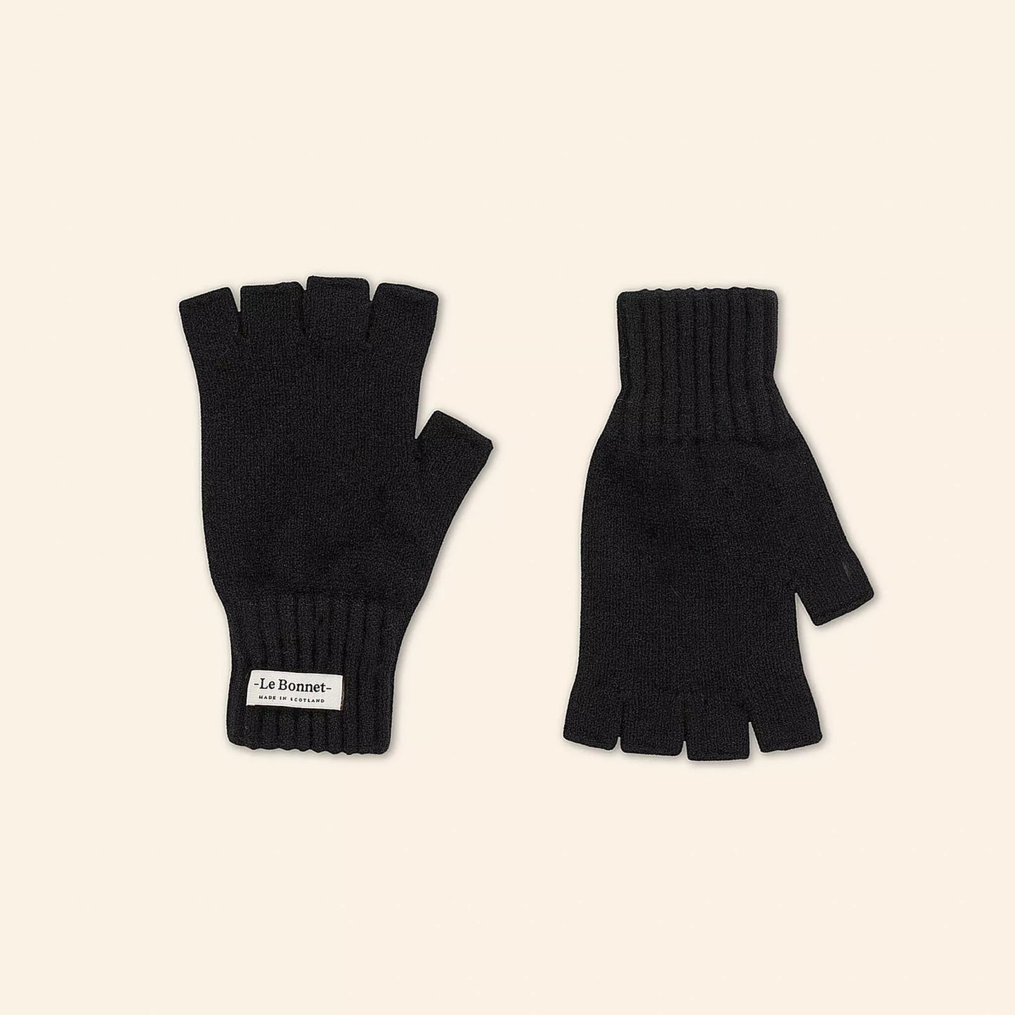 Two Onyx fingerless gloves, knitted from luxurious Merino wool for cold days. One glove features a "Le Bonnet" label. Made in Scotland, they blend style and warmth perfectly.