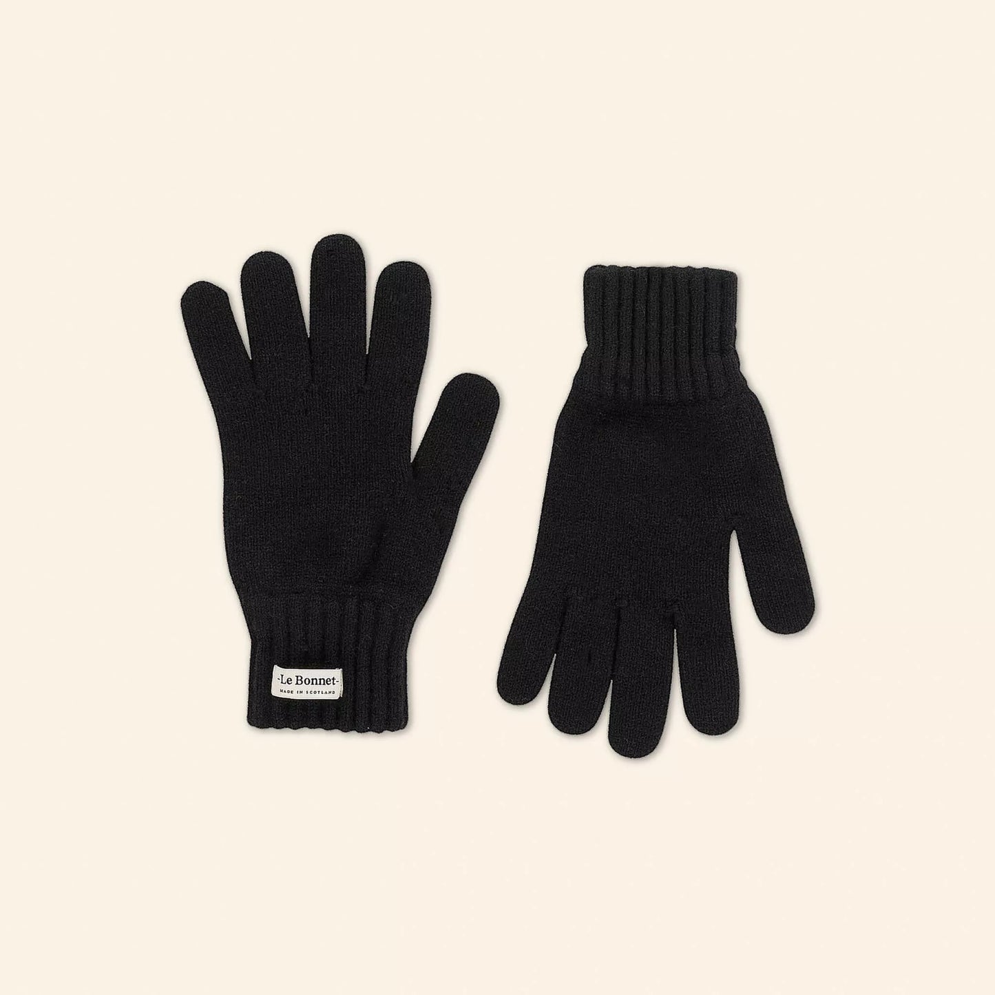 The Gloves, Onyx, by Le Bonnet are black knitted Merino Wool gloves with a visible label on one wrist. Perfect for cold weather, they're displayed against an off-white background.