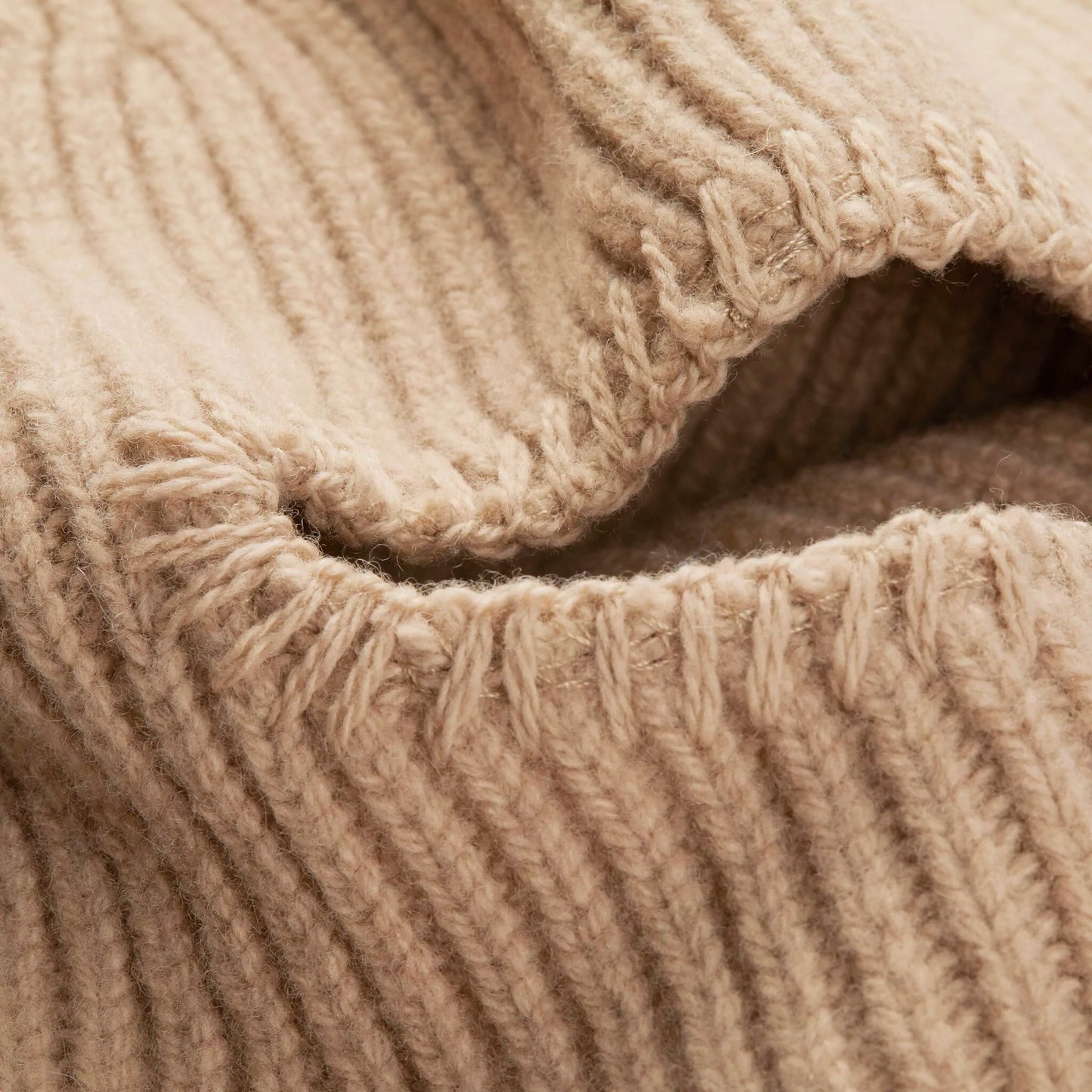 Close-up of the Sand Balaclava by Le Bonnet, highlighting the exquisite texture and detailed stitching of its beige ribbed knit merino wool fabric.