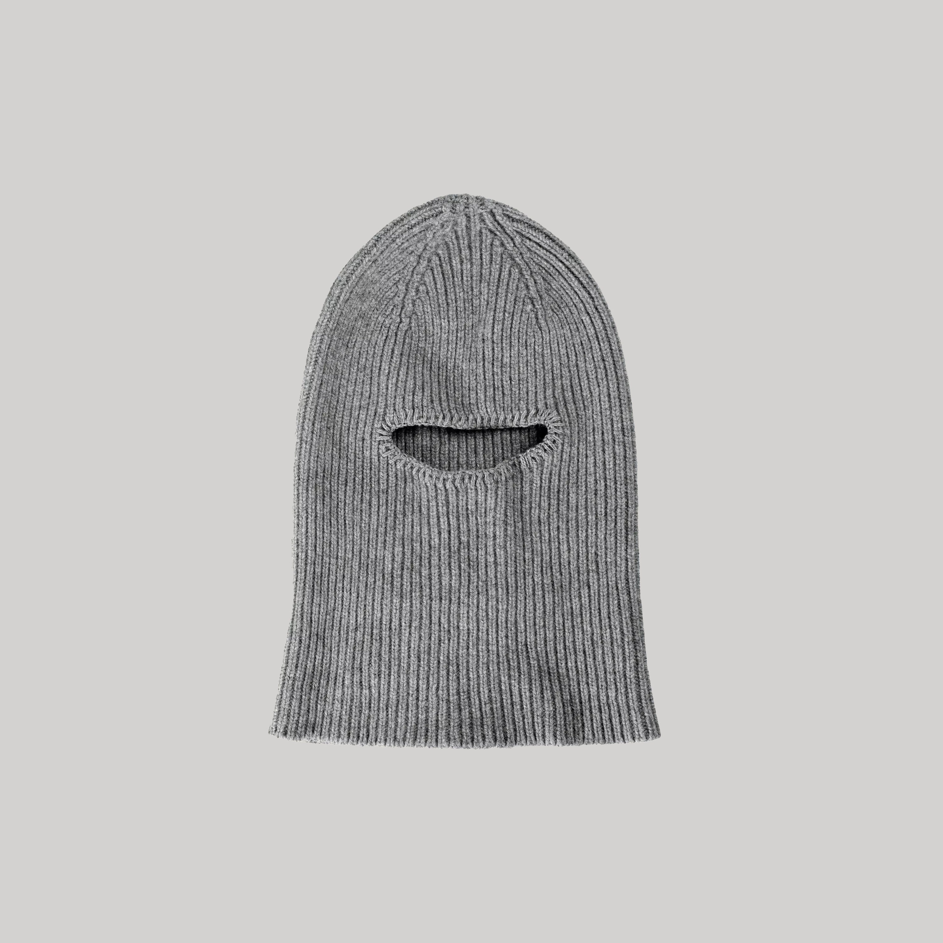 The Smoke Balaclava by Le Bonnet is displayed on a simple background, showcasing its gray ribbed design made from luxurious Merino wool and featuring a single horizontal eye opening.