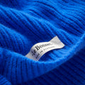 Close-up of a ribbed blue knit fabric, made from biodegradable lambswool, featuring a white label that says "Le Bonnet, Made in Scotland." This fabric is part of the Le Bonnet Scarves collection in Royal Azure.