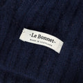 Close-up of a fabric label on the dark wool Beanie, Midnight by Le Bonnet, displaying "Le Bonnet - Made in Scotland." Crafted from soft lambswool, this beanie highlights exceptional Scottish craftsmanship.