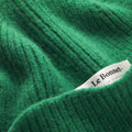 This close-up of a green ribbed knit fabric showcases the luxurious "Scarves, Pine" by Le Bonnet, crafted from biodegradable lambswool for style and sustainability.