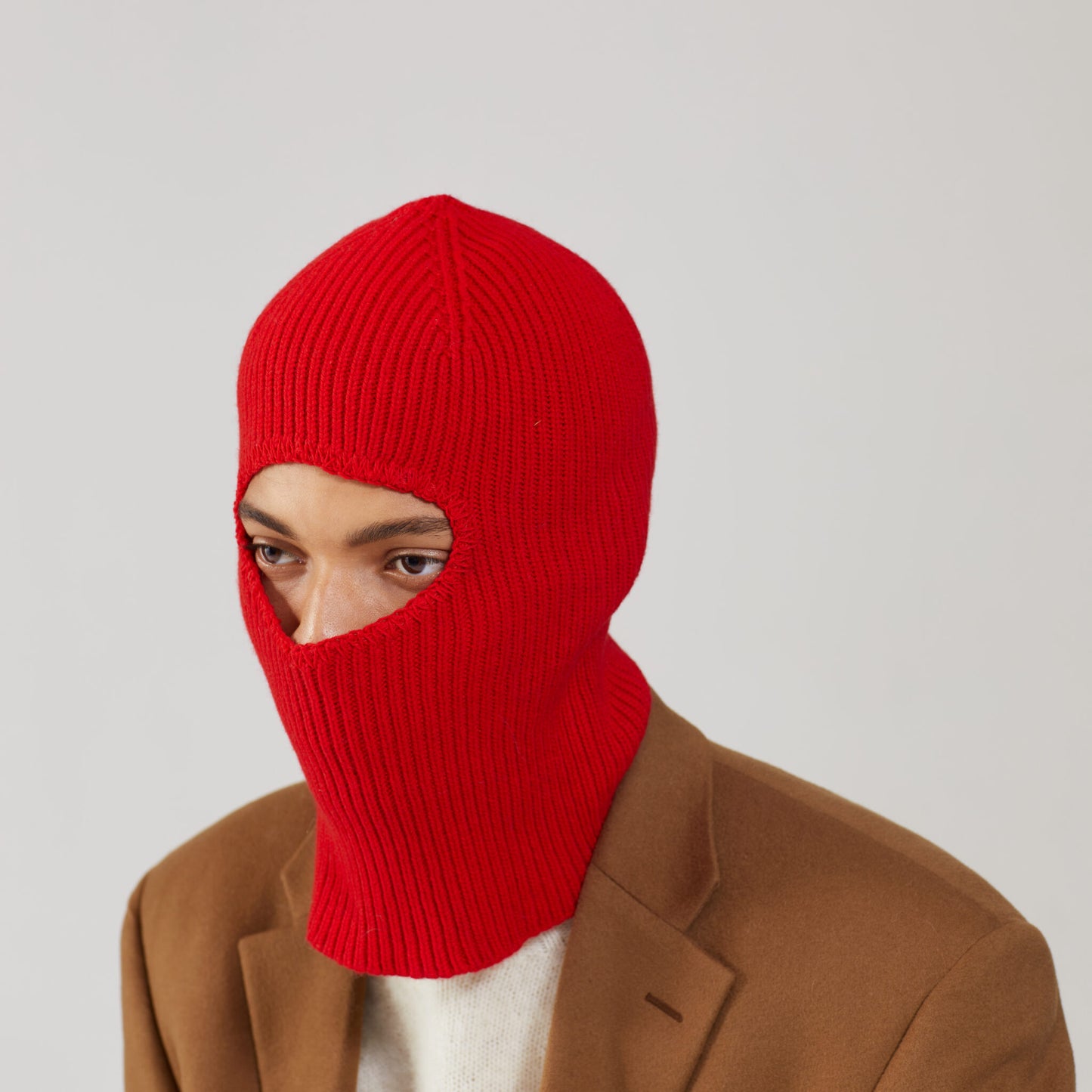 A person wearing Le Bonnet's limited edition Crimson balaclava in merino wool and a brown coat, facing slightly left.