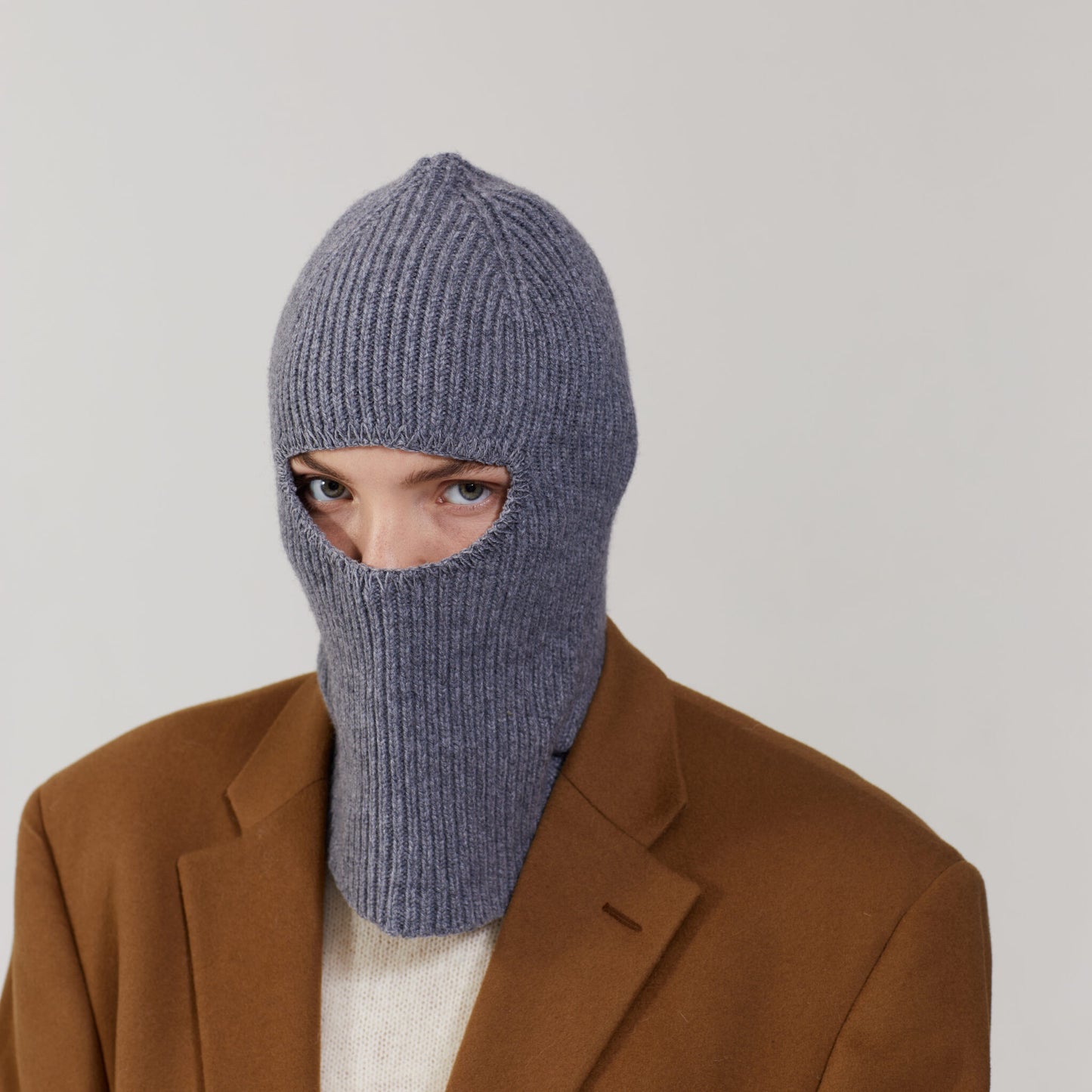 A person in a brown coat and a Le Bonnet Smoke balaclava, made of lavish Merino wool, looking at the camera.