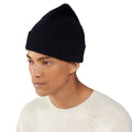 Wearing a Le Bonnet Beanie and a white sweater, a person gazes to the side against a plain background.