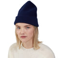 A person is wearing a dark blue Le Bonnet lambswool beanie and a white sweater against a plain background.