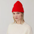 A Le Bonnet "Crimson" beanie complements the outfit alongside a cream sweater, as the person poses against a plain background.