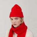 A person in a red knit hat and matching Le Bonnet Crimson lambswool scarf over a cream sweater gazes at the camera with a neutral expression.