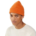 A person wearing a comfortable orange Le Bonnet Beanie and a light-colored sweater stands against a plain background.