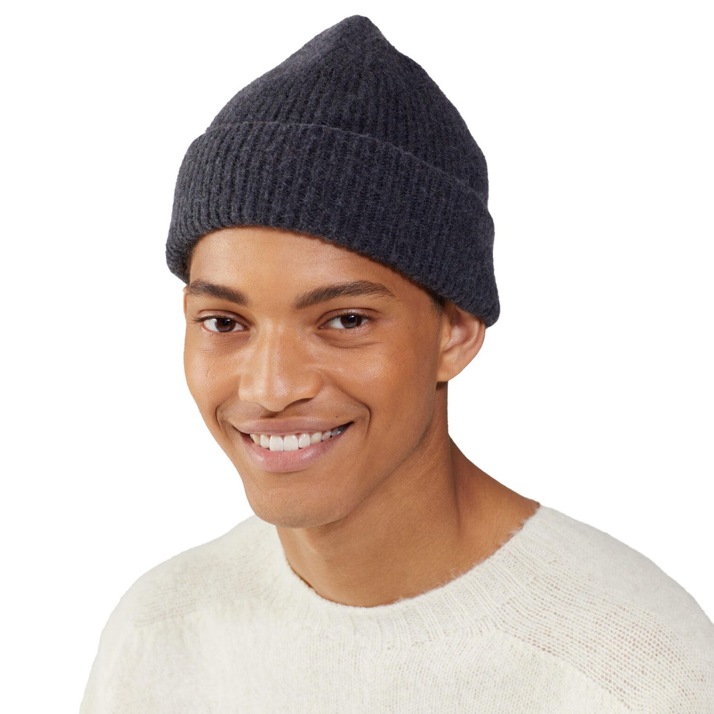 A person wearing a dark Le Bonnet beanie and a light sweater smiles warmly at the camera against a plain background.