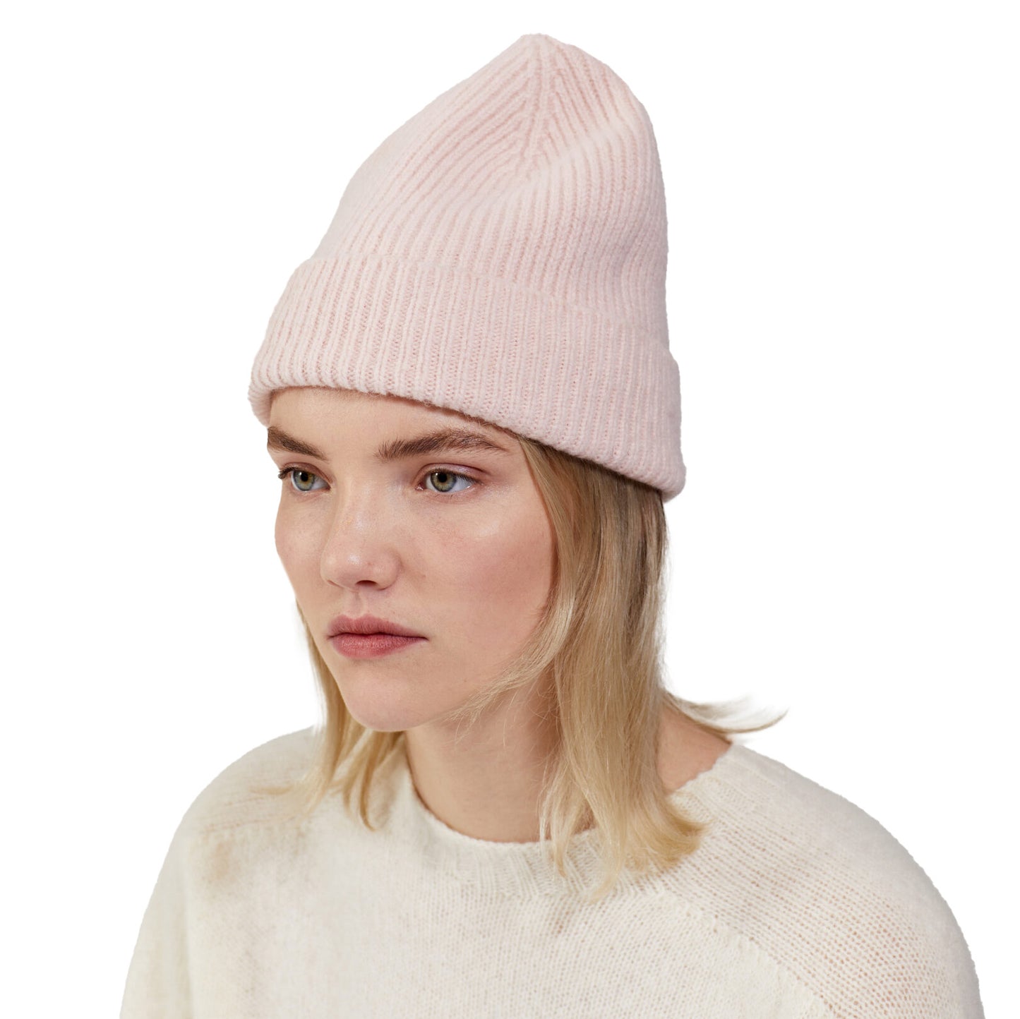 A person with blonde hair is wearing a pink ribbed Beanie by Le Bonnet and a cream lambswool sweater, looking to the side.