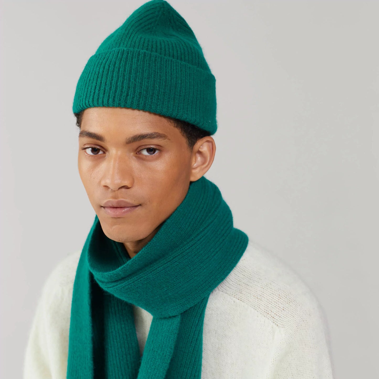 A person wearing a Le Bonnet Pine scarf and matching beanie with a cream sweater stands against a plain background.