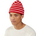 A person wearing a Le Bonnet Beanie in a red and white striped design along with a cream sweater, set against a white background.