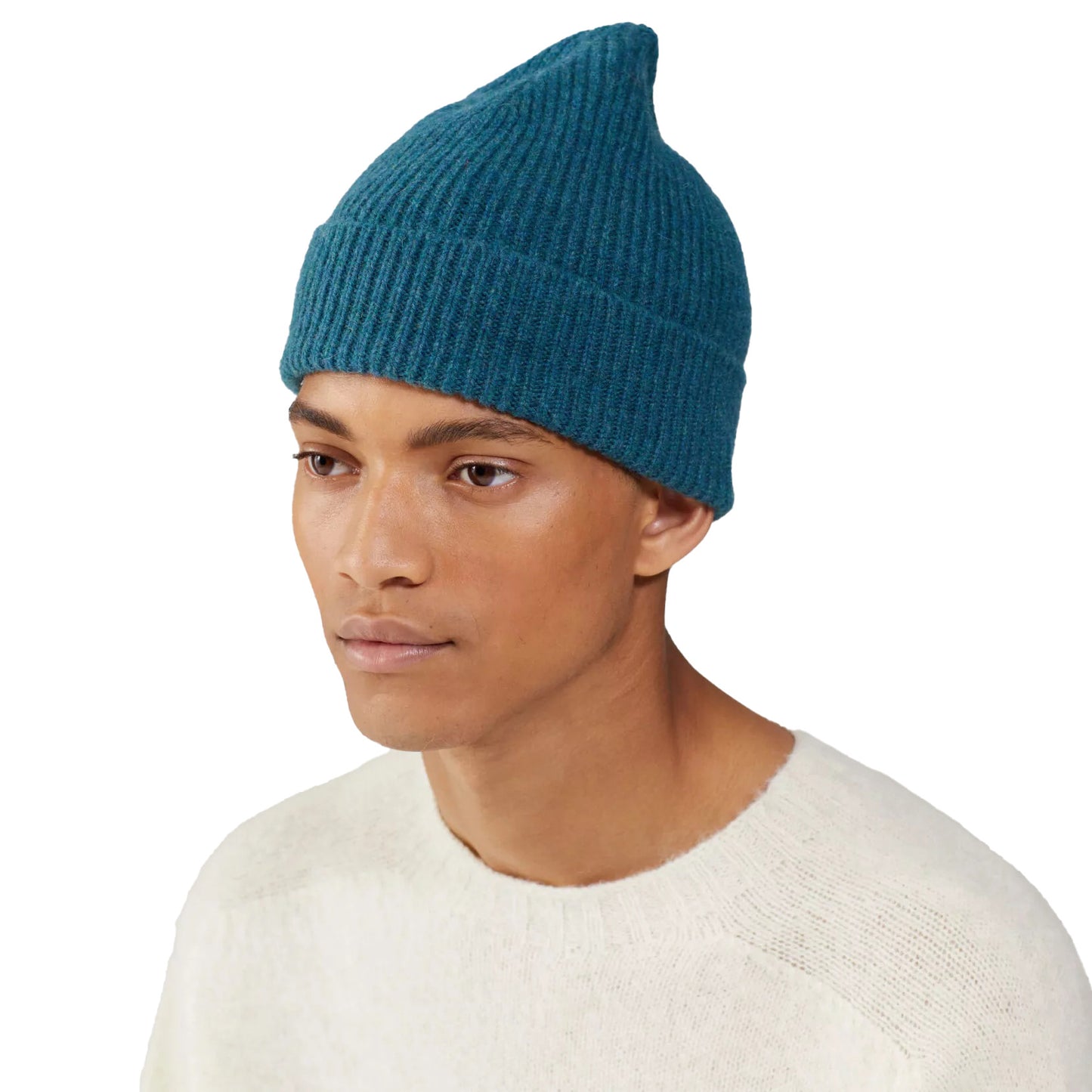 Wearing a teal Le Bonnet ribbed beanie made from lambswool and a cozy white sweater, a person stands against a plain background.