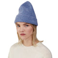 A person with blonde hair is shown wearing a blue Le Bonnet lambswool beanie and a cream sweater, looking directly at the camera against a plain white background.