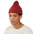 A person wearing a red Le Bonnet lambswool Beanie with a pointed top and a white sweater stands against a plain background.