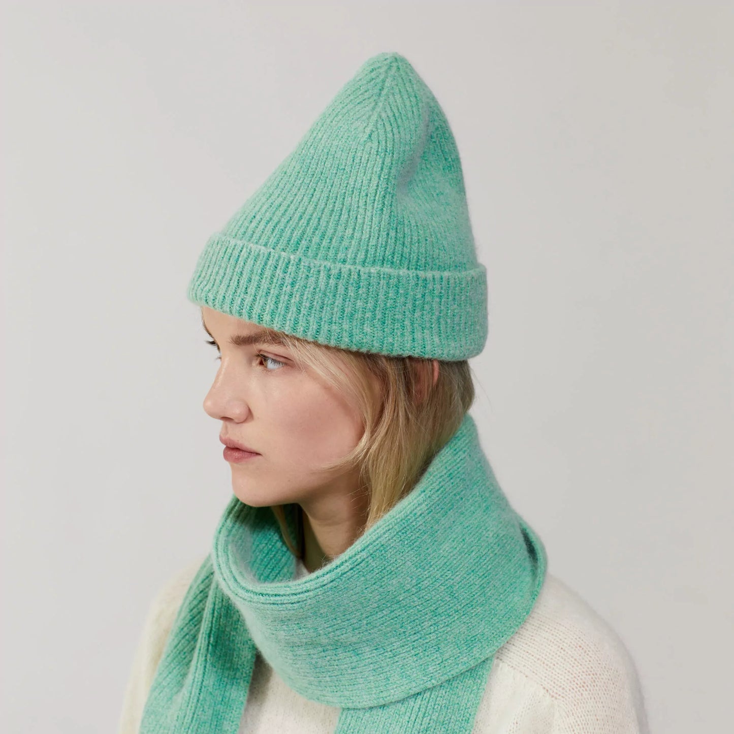 A person wearing a Le Bonnet mint green lambswool knit hat and a Jade scarf, looking to the side.