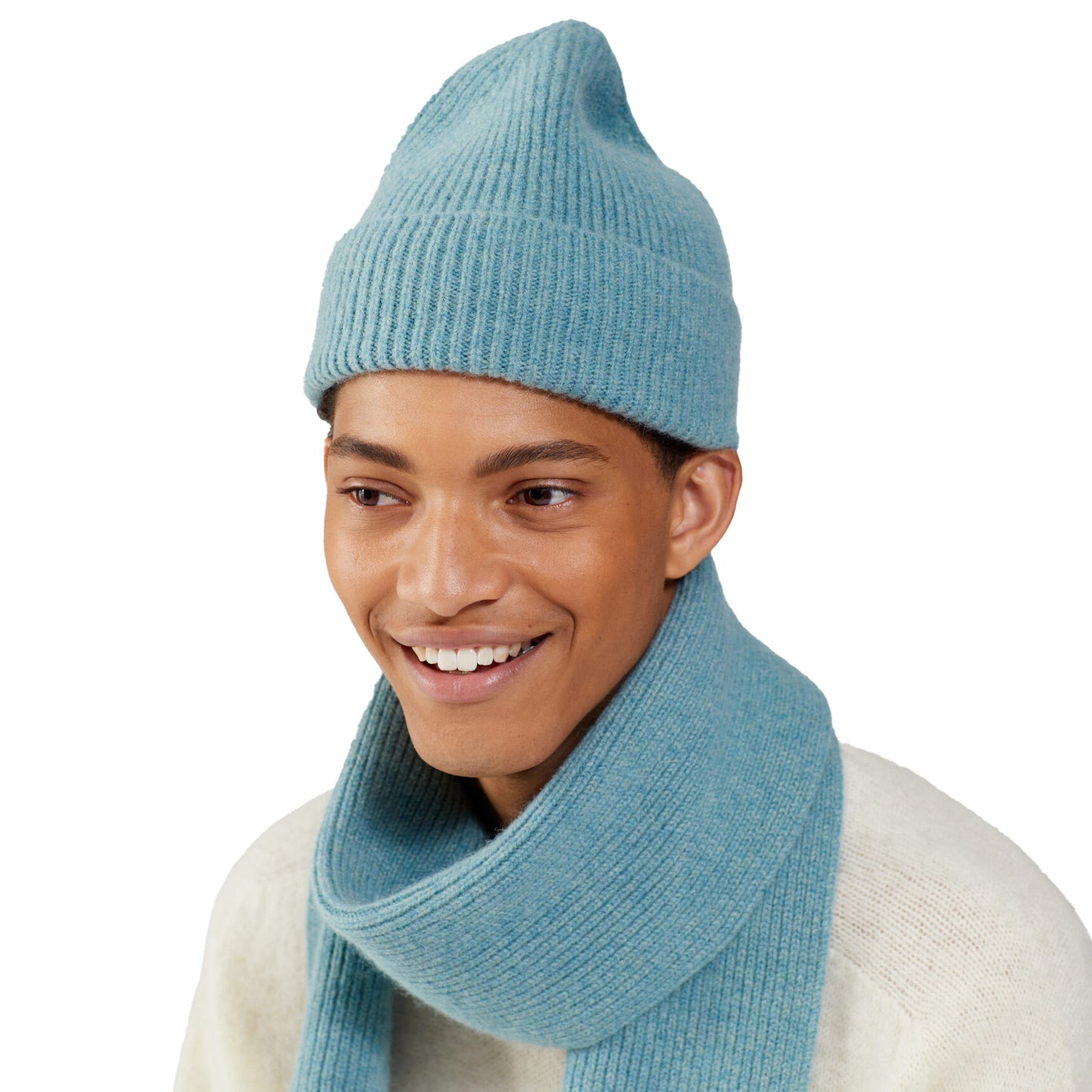 A person wearing a cozy blue Le Bonnet beanie and matching scarf is smiling warmly, set against a crisp white background.