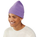 A person wearing a purple Le Bonnet beanie and a cream sweater smiles while looking to the side.