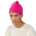 A person wearing a bright pink Le Bonnet beanie and an off-white lambswool sweater stands against a white background.